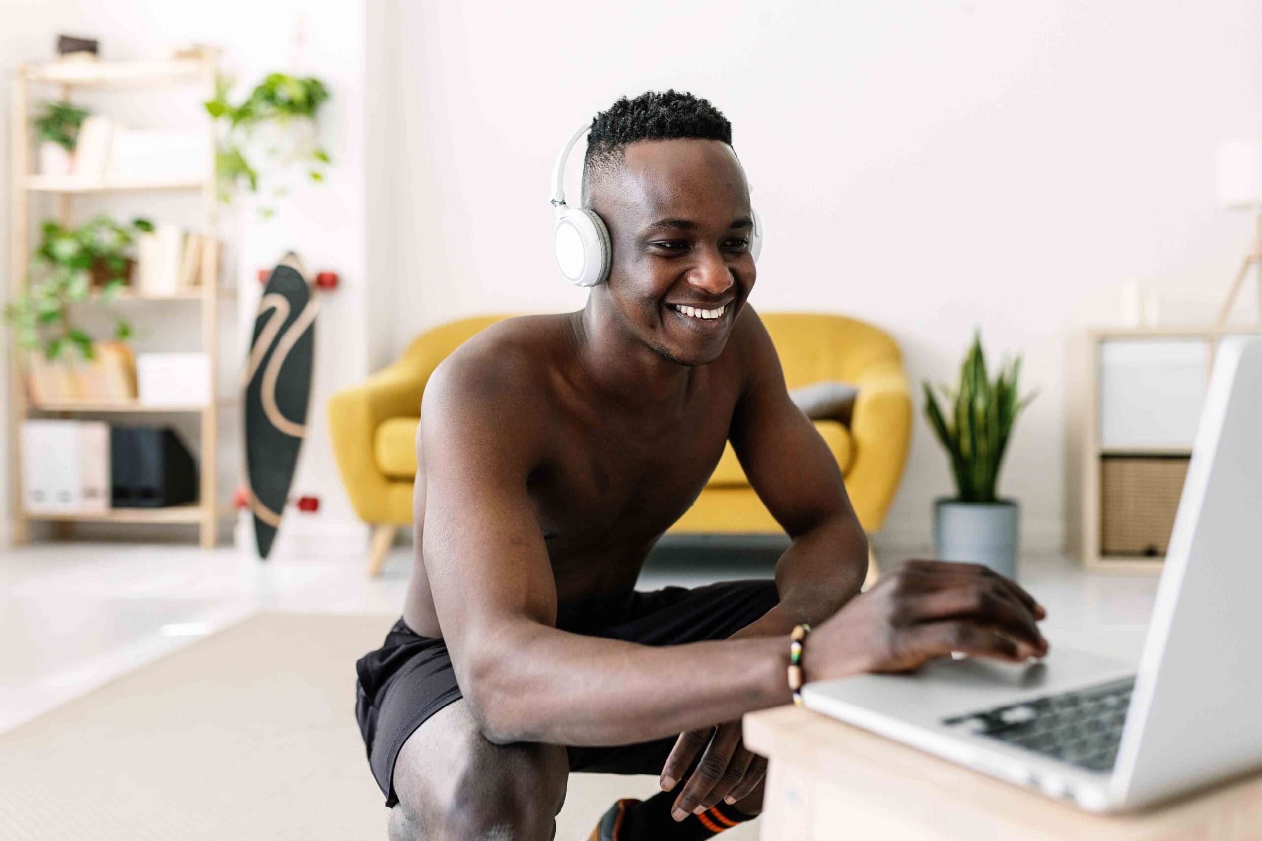 Happy young african man using laptop computer before work out routine at home searching online training fitness tutorial class - Healthy lifestyle and sport concept